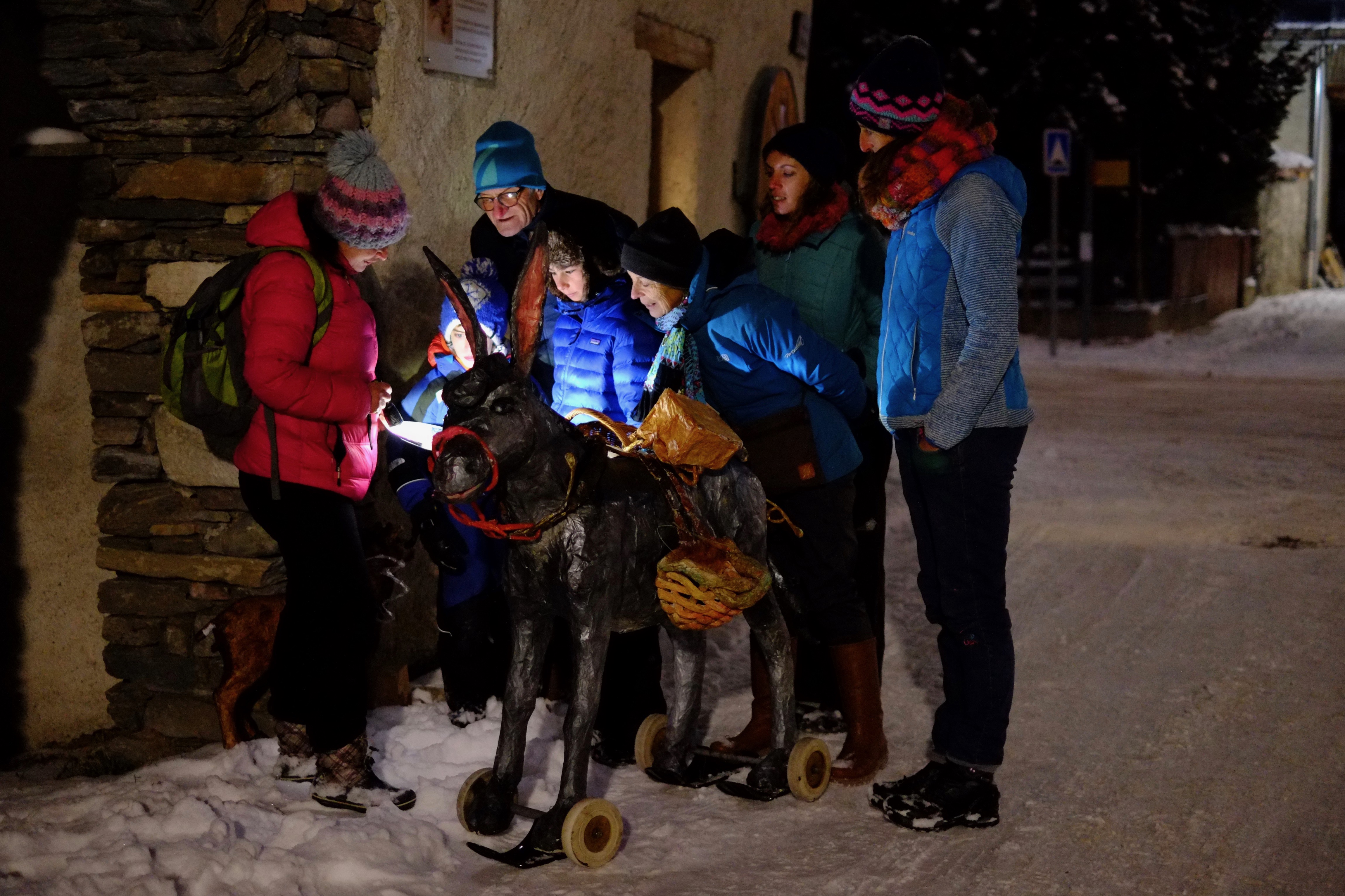 Groupe d'adultes et d'enfants dans un village enneigé autour d'un âne à roulettes